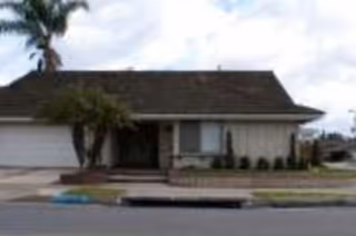 Front exterior of a single-story house with an attached garage, driveway, and palm trees.