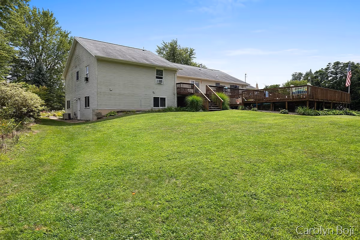 Light-gray house with a large wooden deck overlooking a wide green lawn and trees.