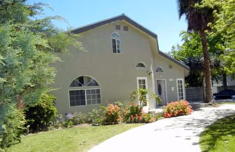 Be Well Senior Living Tarzana exterior: beige building with arched windows, palm trees, and landscaped walkway.