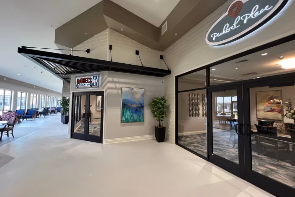 Interior lobby of a senior living community showing the entrance to 'Daniels Theater' with seating areas and glass doors to adjacent rooms.