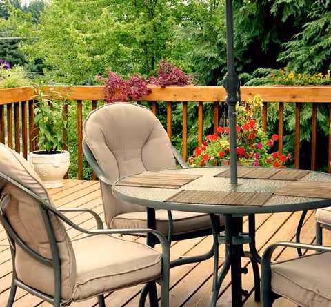 Outdoor wooden deck with round table, chairs, umbrella, and potted plants.