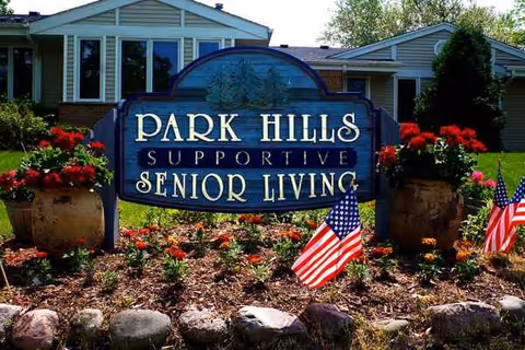 Front yard sign reads Park Hills, Supportive Senior Living, with flowers and a building in background.