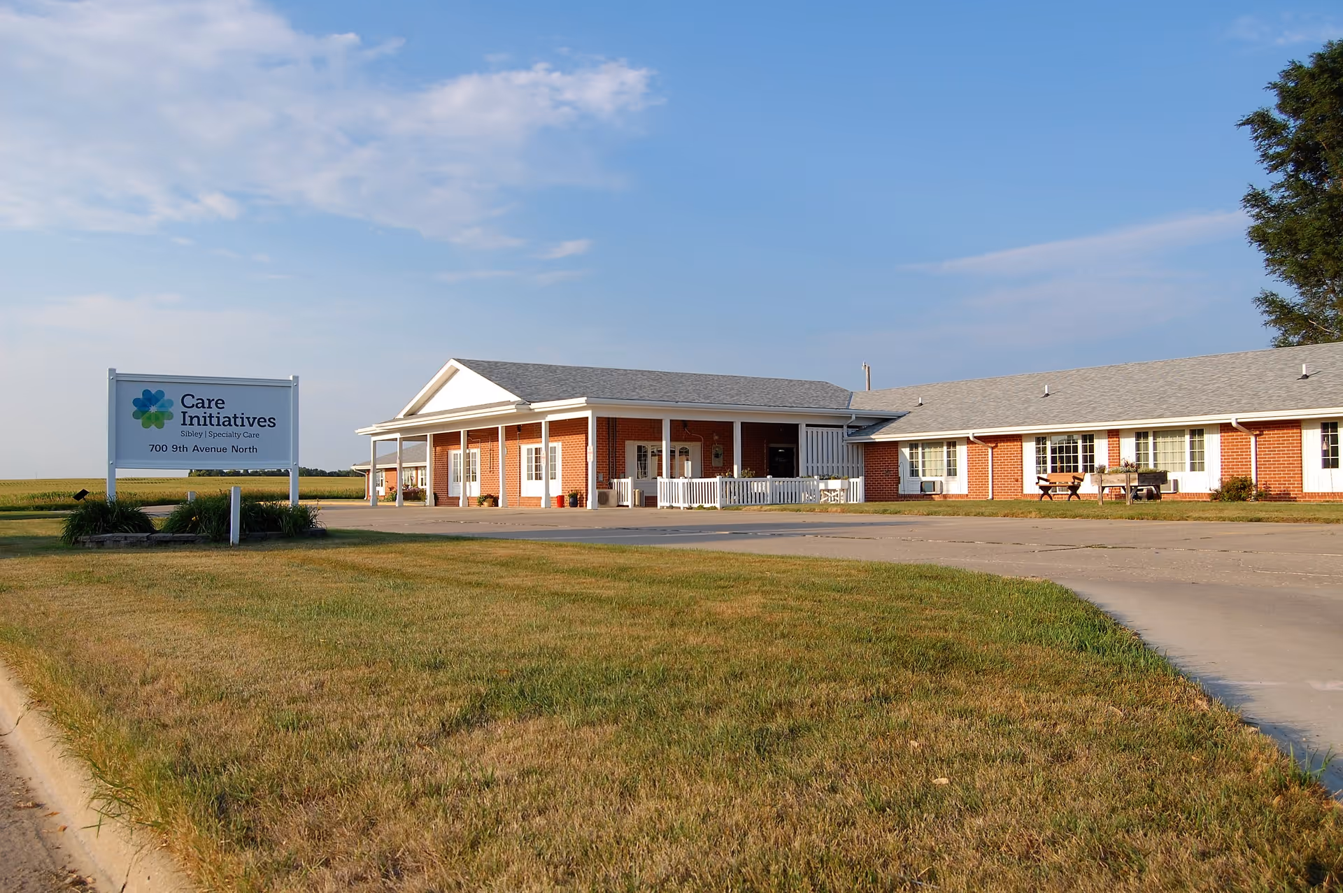 Single-story brick senior care building with a front entrance, driveway, lawn, and a 'Care Initiatives' sign.