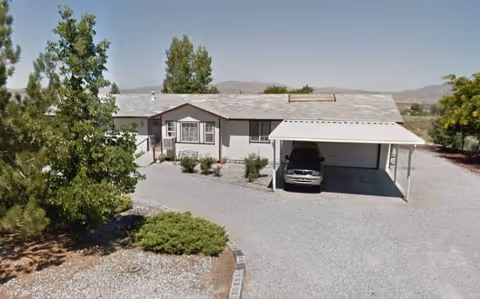 Single-story building with carport, gravel driveway, and desert landscaping.