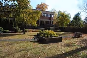 Front of a two-story brick building with a landscaped courtyard featuring raised planters, benches, and trees in autumn.