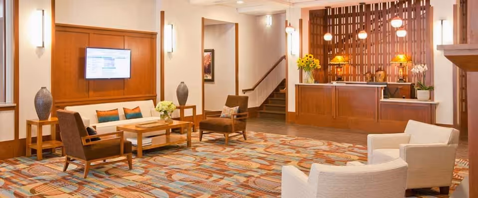 Spacious senior living lobby with seating area, patterned carpet, wall-mounted TV, and a reception desk.