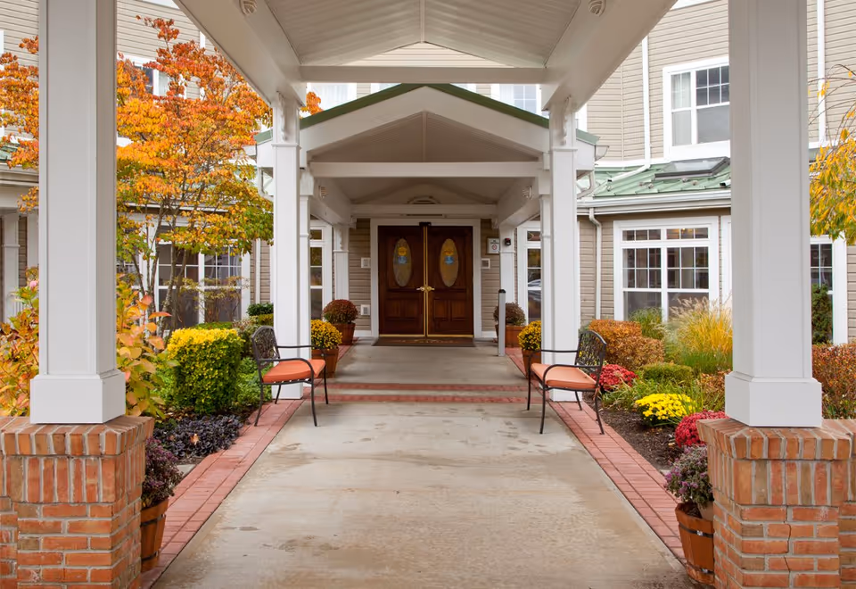 Covered entrance walkway with double wooden doors, benches, and autumn landscaping.