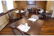 Small dining room with several tables set with napkins and place settings, upholstered chairs, and wood flooring.