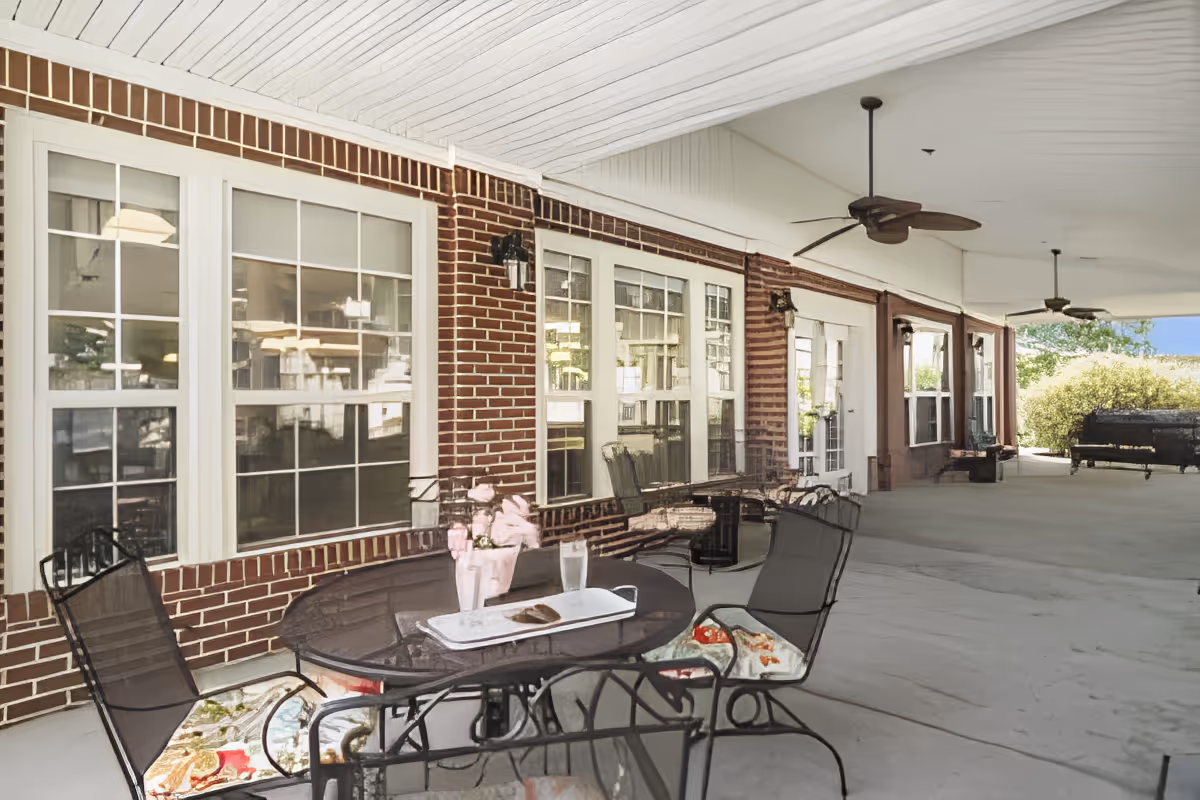 Covered brick patio with an outdoor table and chairs, ceiling fans, and large windows along the building.