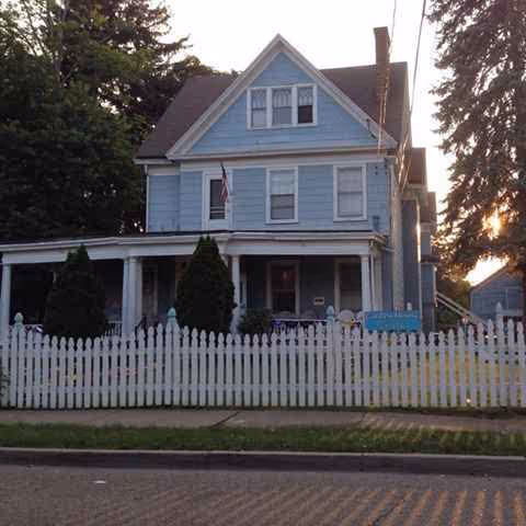 Blue two-story building with white picket fence, front yard, and porch.
