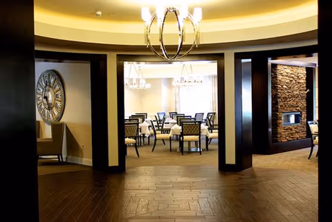 Interior dining lounge with chandeliers, tables and chairs, and a stone fireplace.