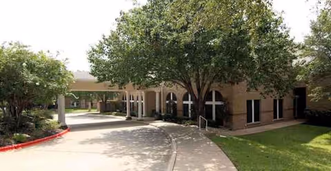 Exterior view of Asher Point Senior Living of Austin with a curved driveway and trees.
