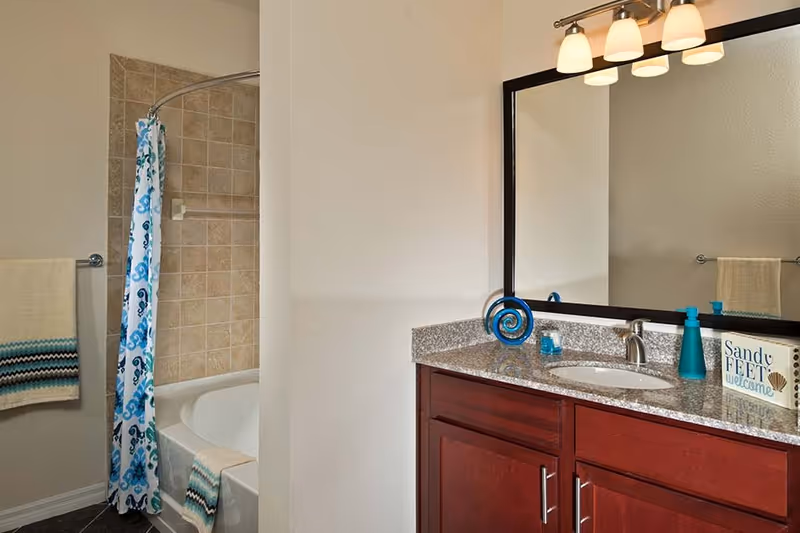 Bathroom featuring a bathtub with tiled shower and blue-patterned curtain, and a granite-top vanity with sink, mirror, and decorative towels.