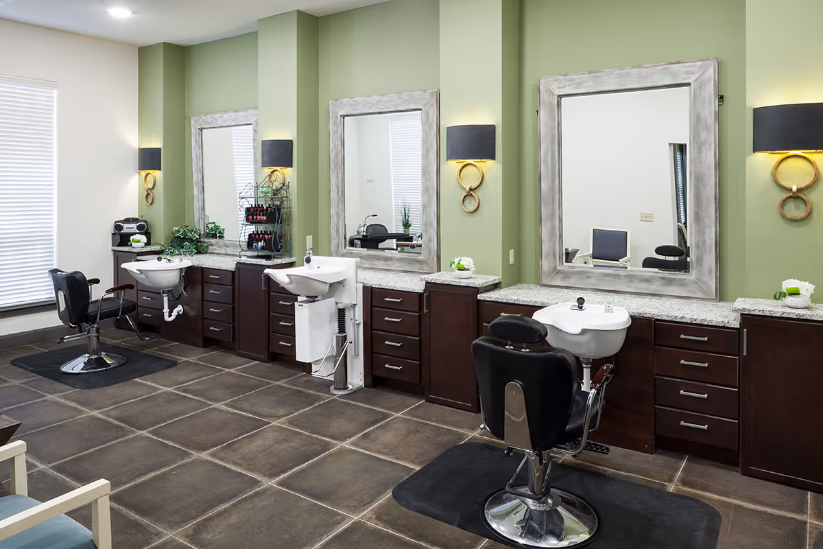 Bright salon room with multiple styling stations, swivel salon chairs, wash basins and large mirrors against green walls.