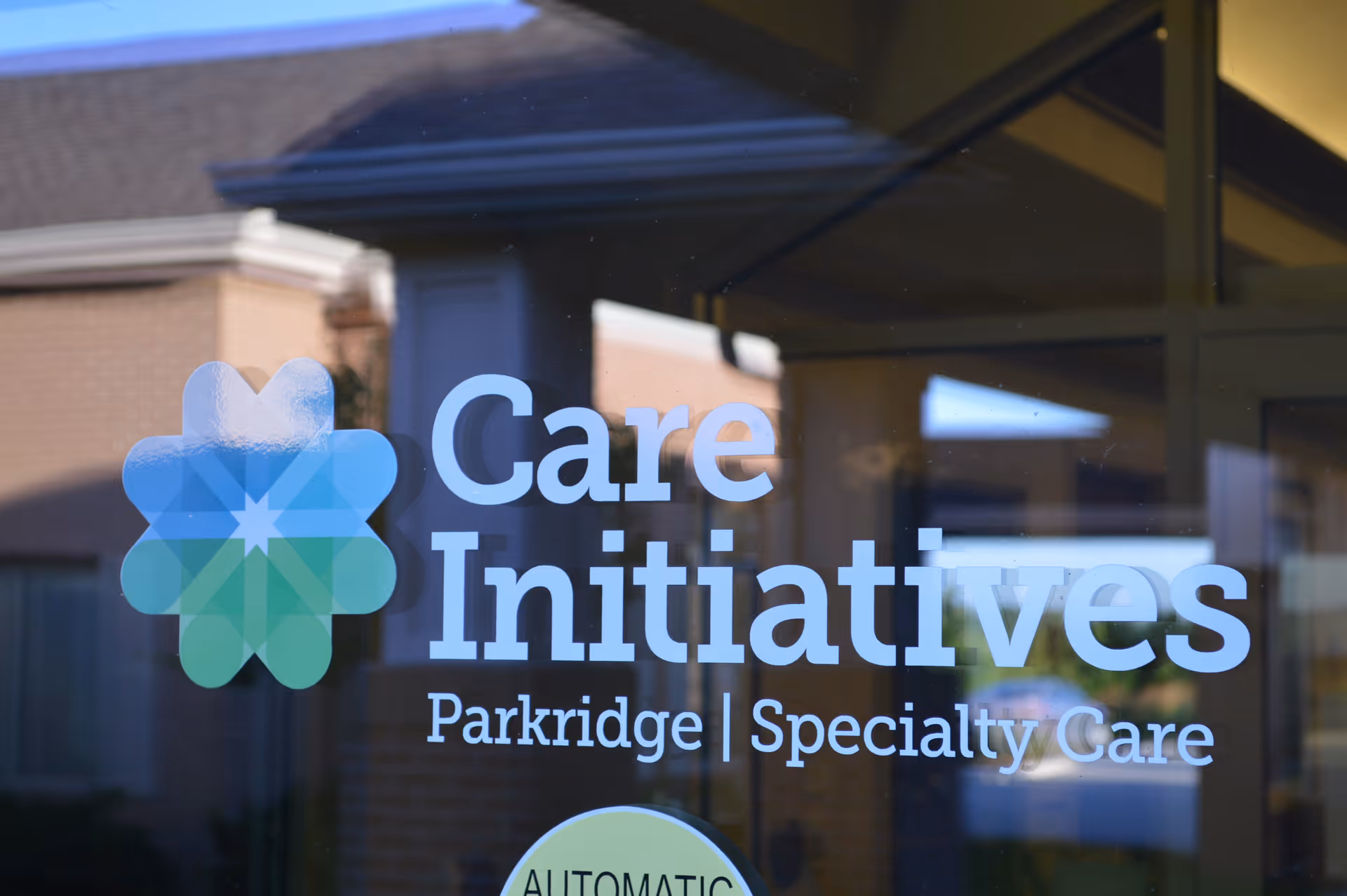 Glass door with the logo and text 'Care Initiatives Parkridge | Specialty Care' printed on it, reflecting the exterior of a building.