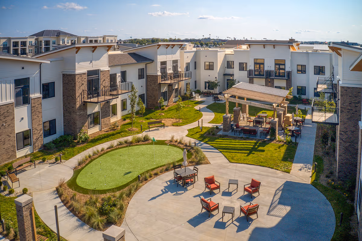 A landscaped central courtyard at Preston Greens Senior Living with seating areas, a small putting green, a pergola, and surrounding two-story residential buildings.