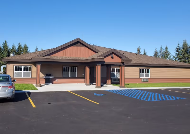 Single-story brown and red building with a covered entrance, parking lot, and marked handicap spaces under a clear blue sky.