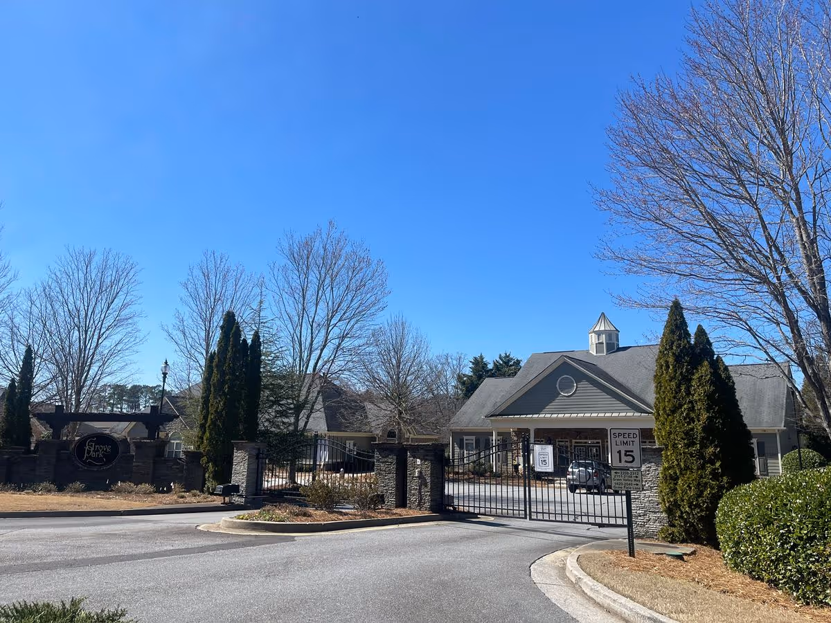 Gated entrance and front building of Grove Park with a driveway, landscaping, and a clear blue sky.
