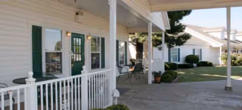 White siding senior living facility exterior with green doors, porches, and outdoor seating.