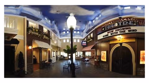 Indoor common area designed to look like an outdoor street scene with a blue sky ceiling, street lamp, benches, storefronts, and a theater marquee showing 'Gone With The Wind'.