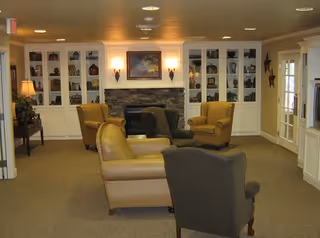 Cozy communal sitting area with armchairs arranged around a stone fireplace and built-in bookshelves.
