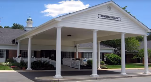 Front entrance with white columns and a covered drop-off area at a senior living facility.