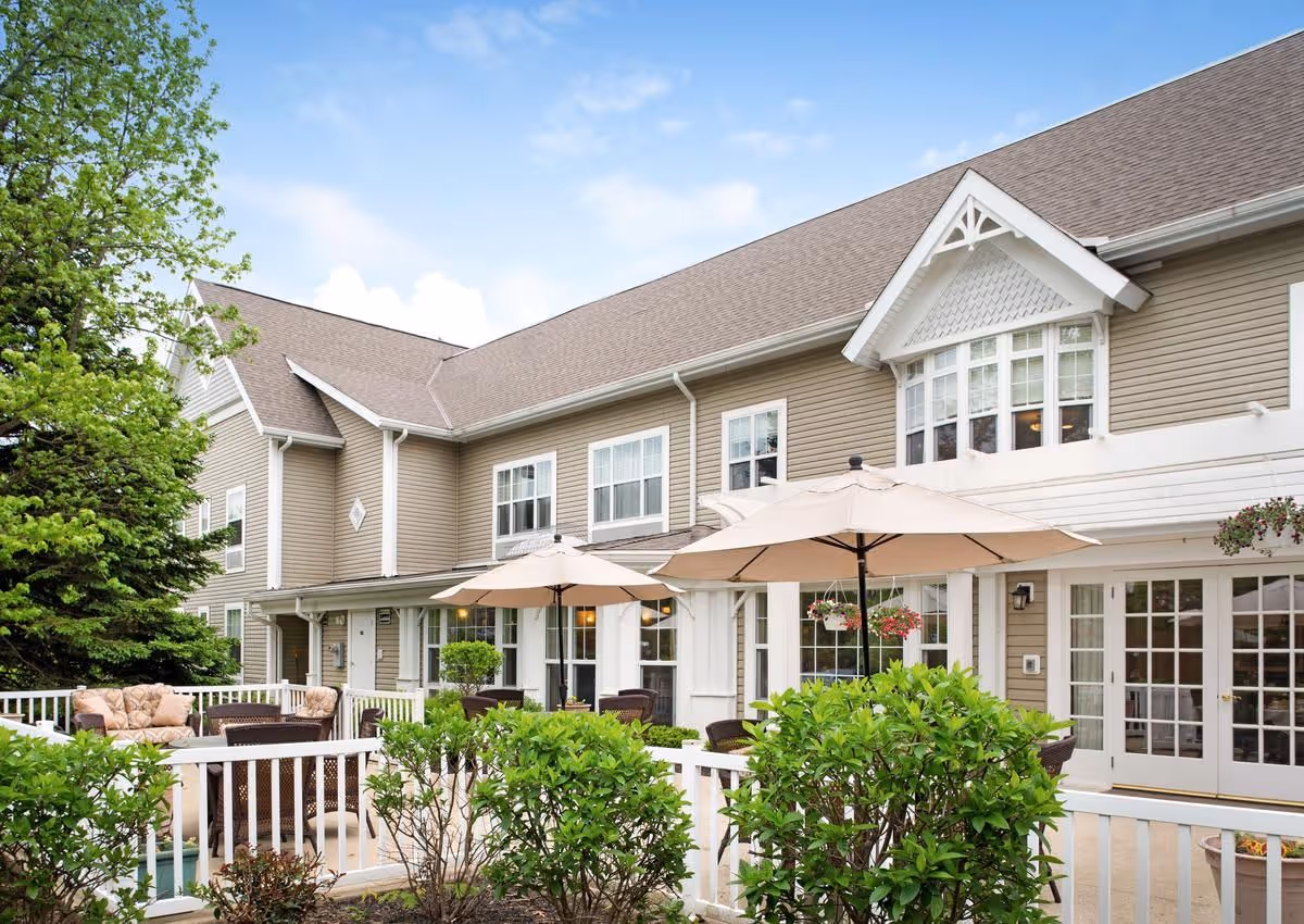 Exterior front of a two-story senior living building with a patio area, umbrellas, and outdoor seating.