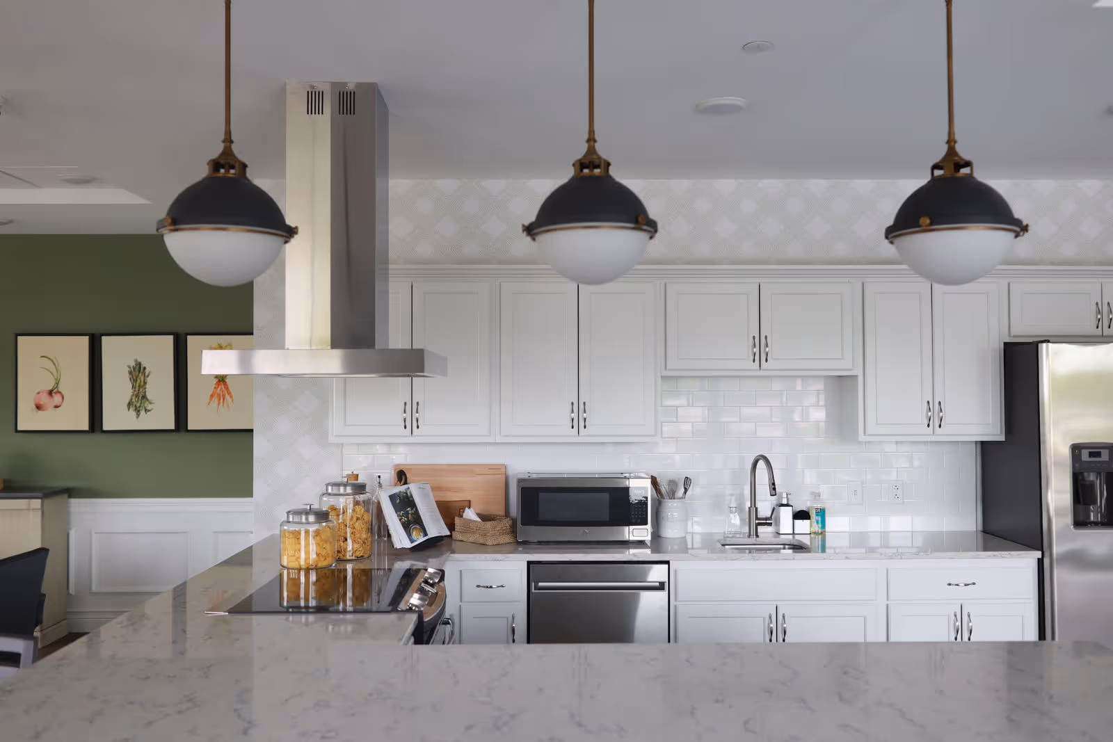 Bright modern kitchen with white cabinetry, marble countertops, three pendant lights, and stainless steel appliances.