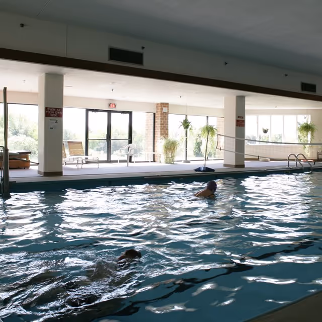 Indoor pool area at Sherwood Oaks with swimmers and lounge seating by windows.
