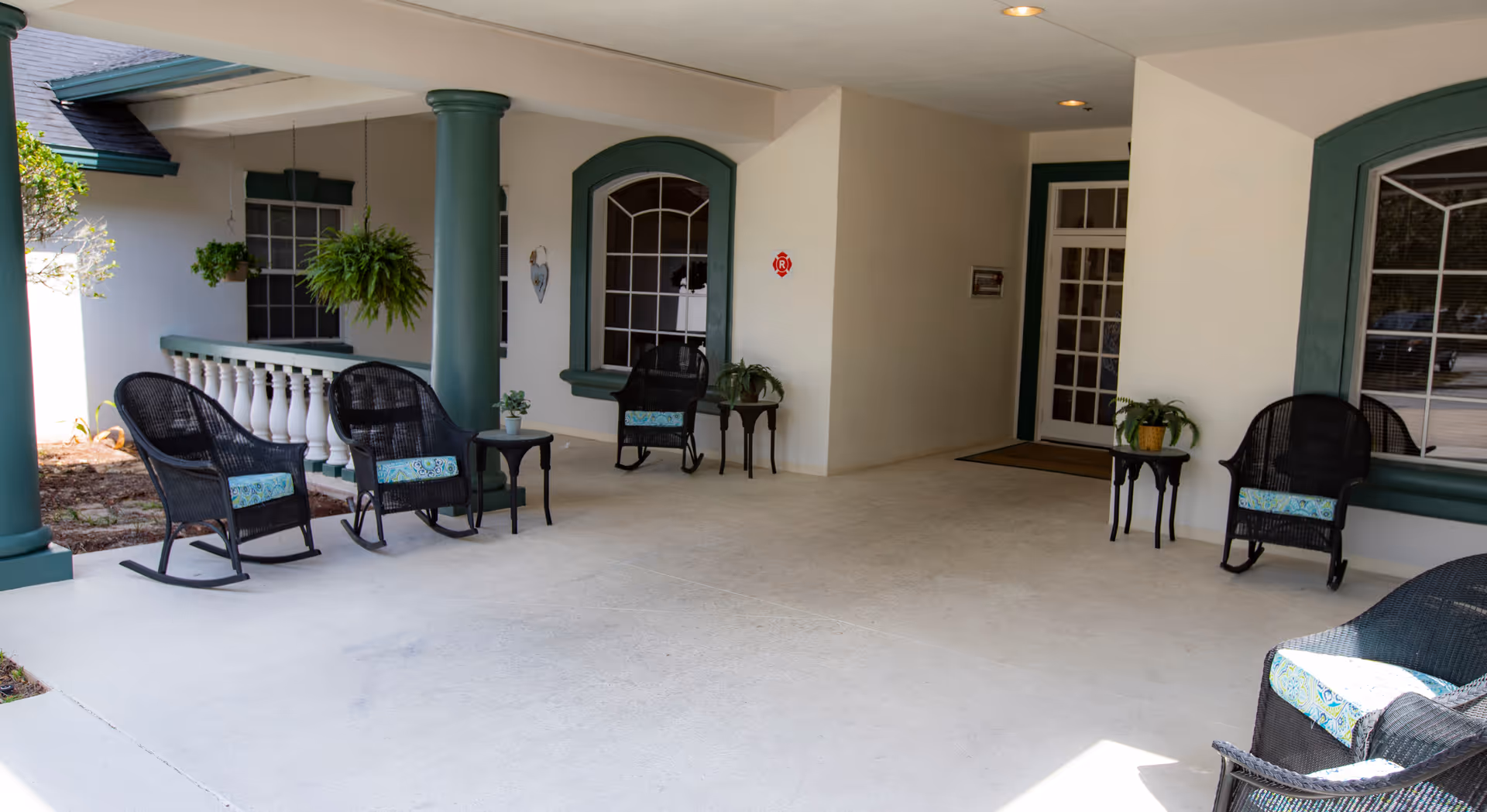 Covered front porch entrance with wicker rocking chairs, columns, potted plants and arched windows.