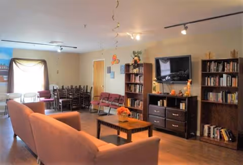 Cozy common living room in a senior facility with couches, bookshelves, and a TV.