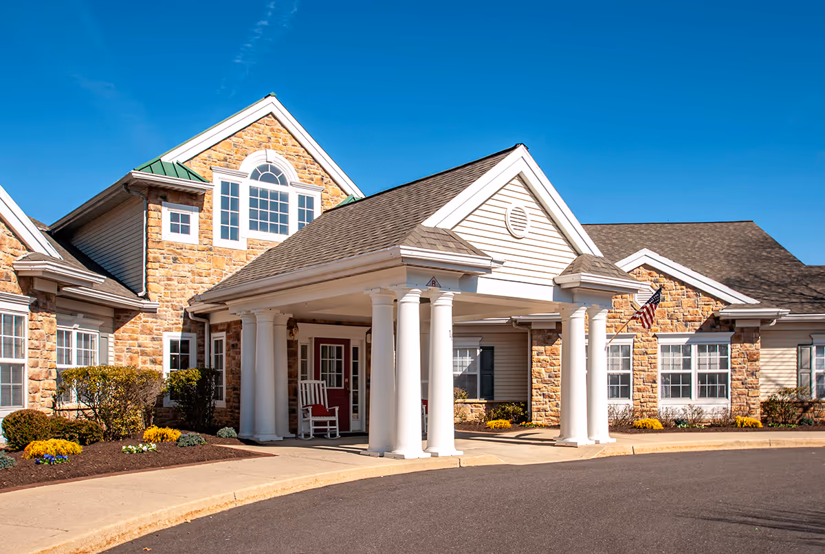 Front entrance of a stone and siding senior living facility with white columns and a driveway.