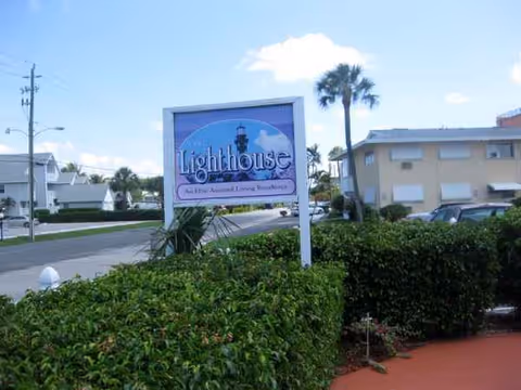 Exterior view of the Lighthouse Inn senior living facility sign beside hedges and a street.