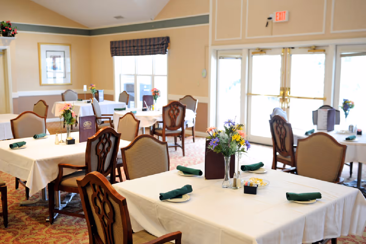 Bright dining room with tables covered in white tablecloths, green napkins, and floral centerpieces.