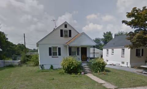 Front view of a white, two-story building with stairs, shutters, and a green lawn.