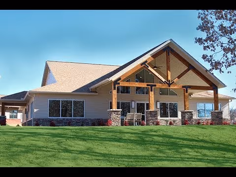Single-story senior living building with a covered timber-beam entrance and green lawn under a clear blue sky.
