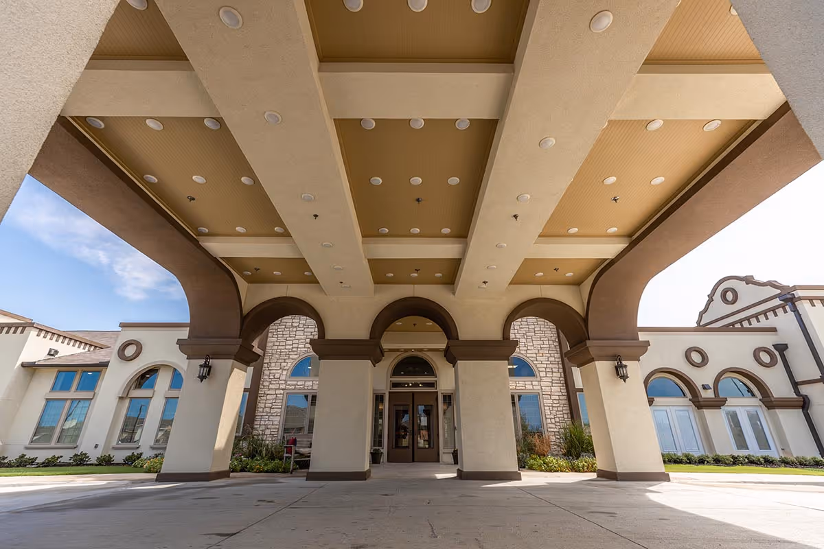 Front entrance canopy with arched columns and glass doors of a senior living facility.