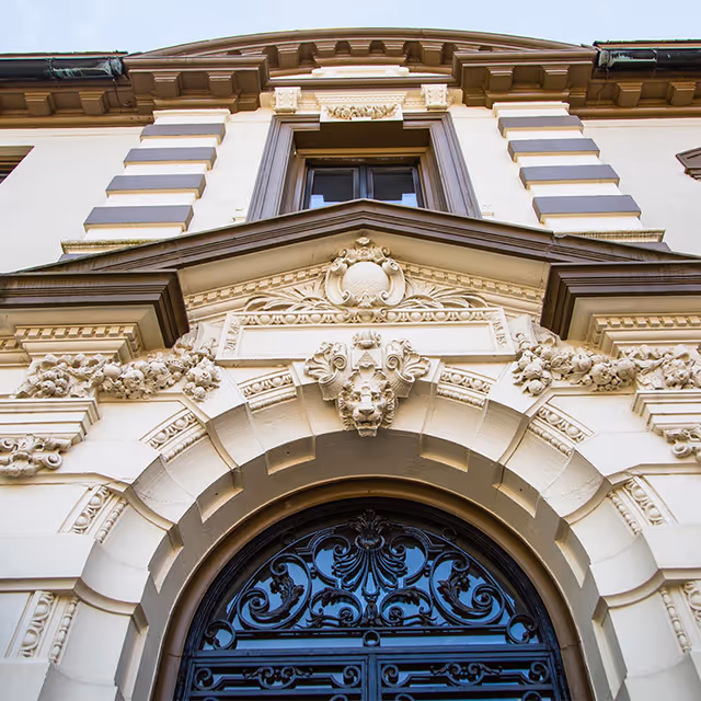 Ornate arched entrance and facade of a historic mansion with decorative stone carvings and an iron door.