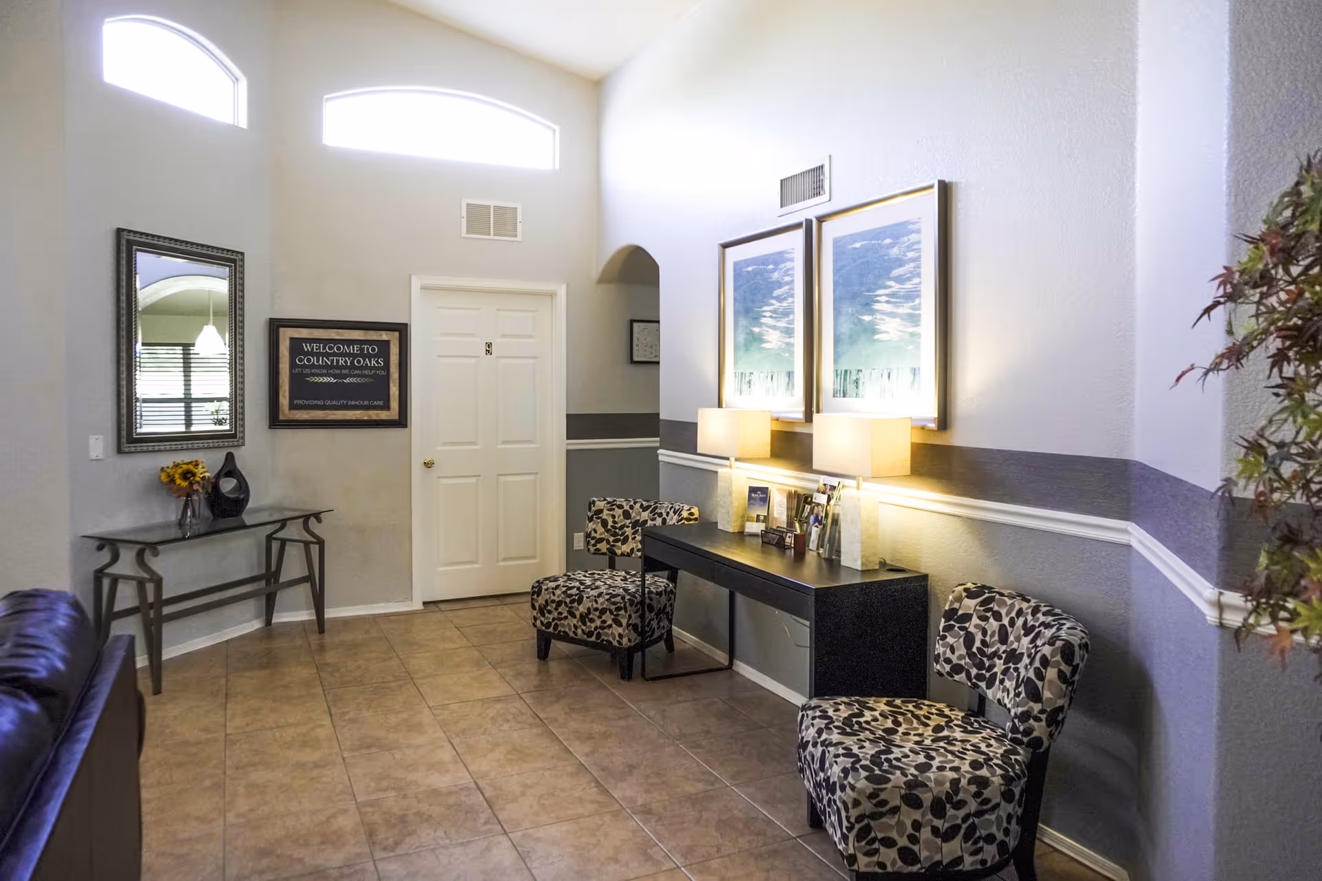 A bright interior reception area with patterned chairs, a long console with lamps and framed art, and a 'Welcome to Country Oaks' sign.