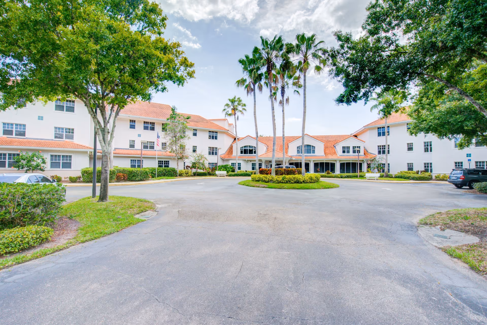 Front exterior of a three-story white senior living building with a circular driveway and palm trees.