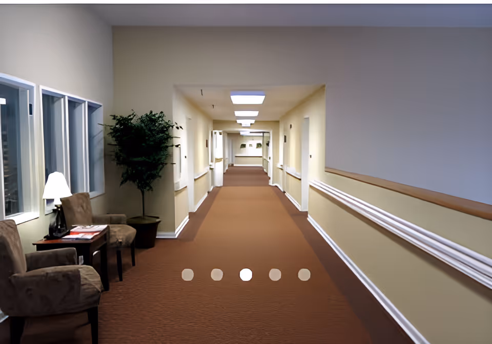 Long carpeted interior hallway with seating and a side table on the left and handrails along the walls.