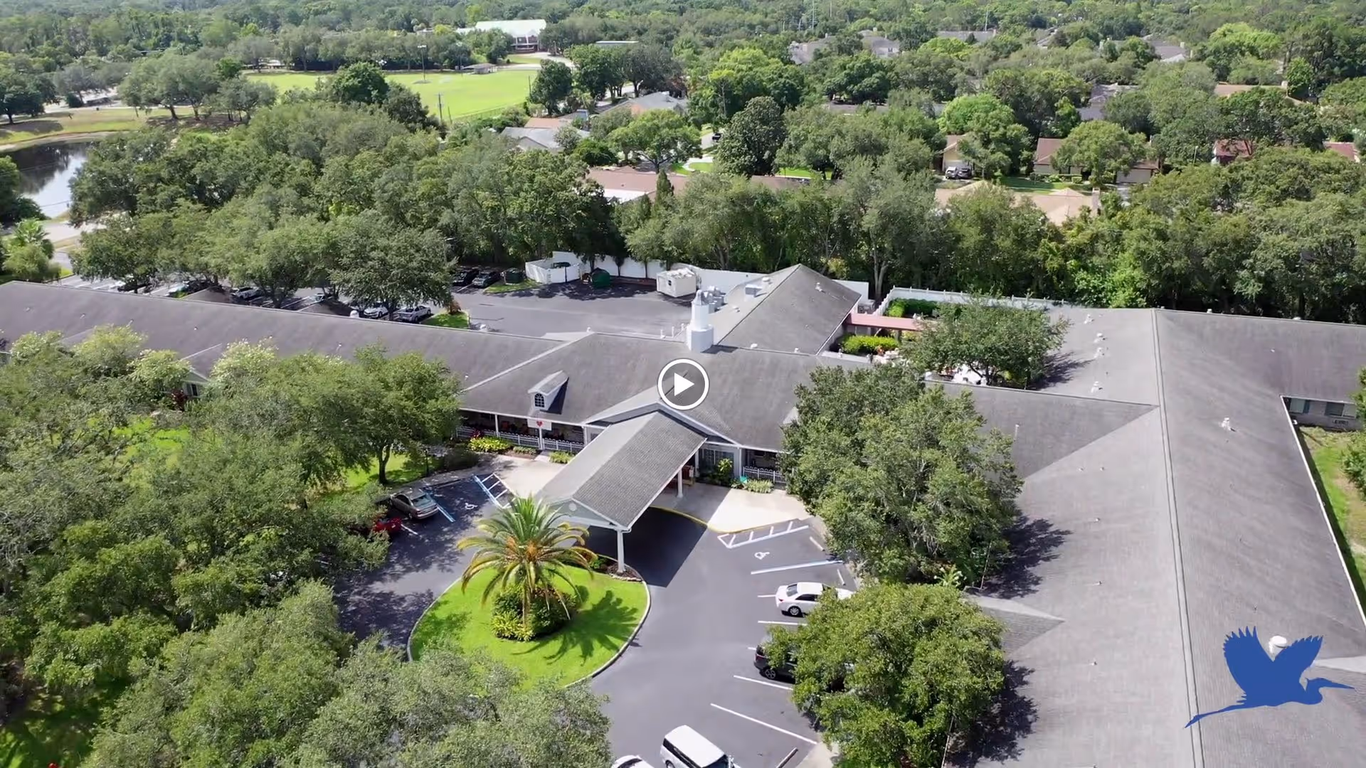 Aerial view of a single-story senior living facility with a covered entrance, circular driveway, parking lot, and surrounding trees.