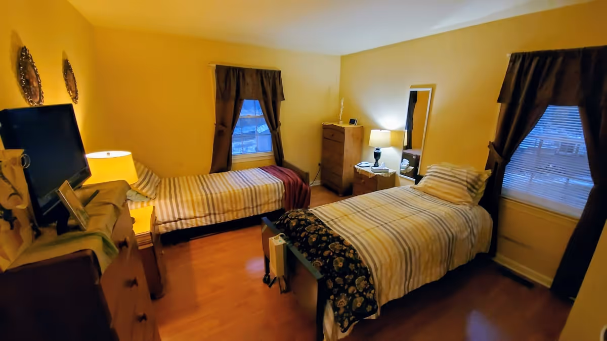 A cozy bedroom with two twin beds, striped bedding, dressers, lamps, and curtained windows.