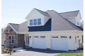 Front exterior of a light-colored residential building with a three-car garage, gabled roof, and stone accents.