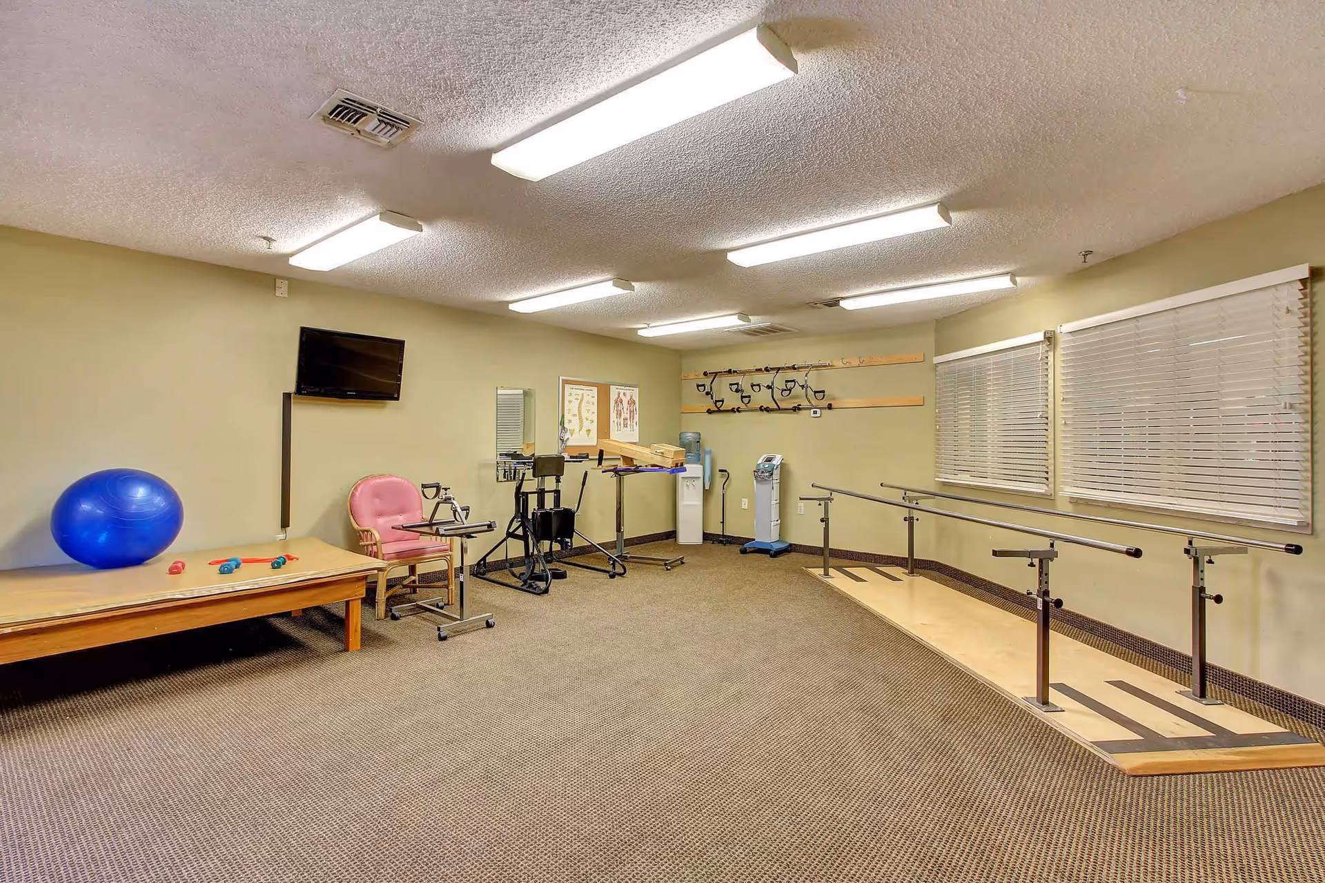 Rehabilitation/exercise room with parallel bars, therapy equipment, an exercise ball, and a TV.