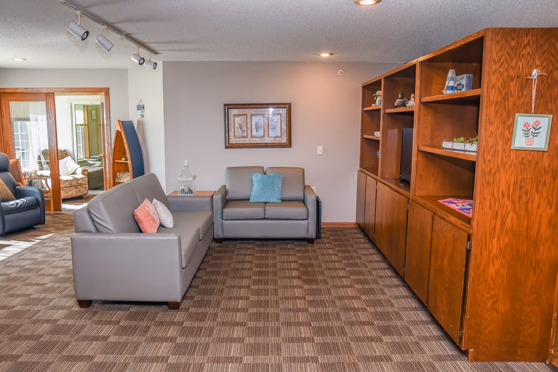A cozy common living room with two gray sofas, built-in wooden shelving, and framed art on the wall.