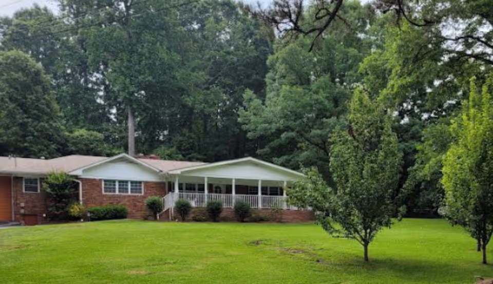 Single-story brick senior care home with a white front porch, surrounded by green lawn.