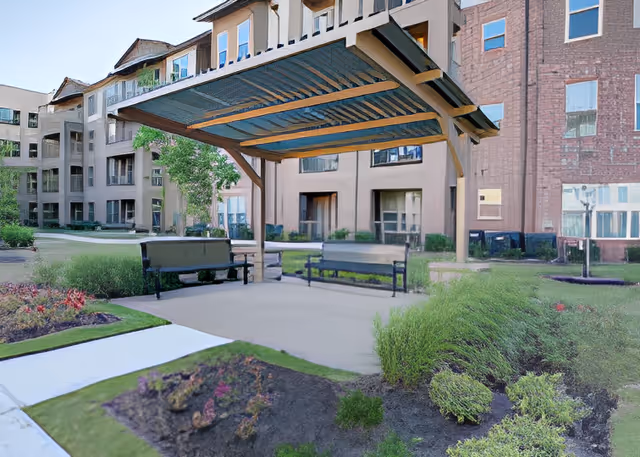 Outdoor courtyard with a covered pergola and benches in front of a multi-story senior living building.