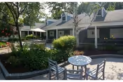 Outdoor courtyard patio with a round table and chairs, landscaped garden beds, and a single-story building with covered walkways.