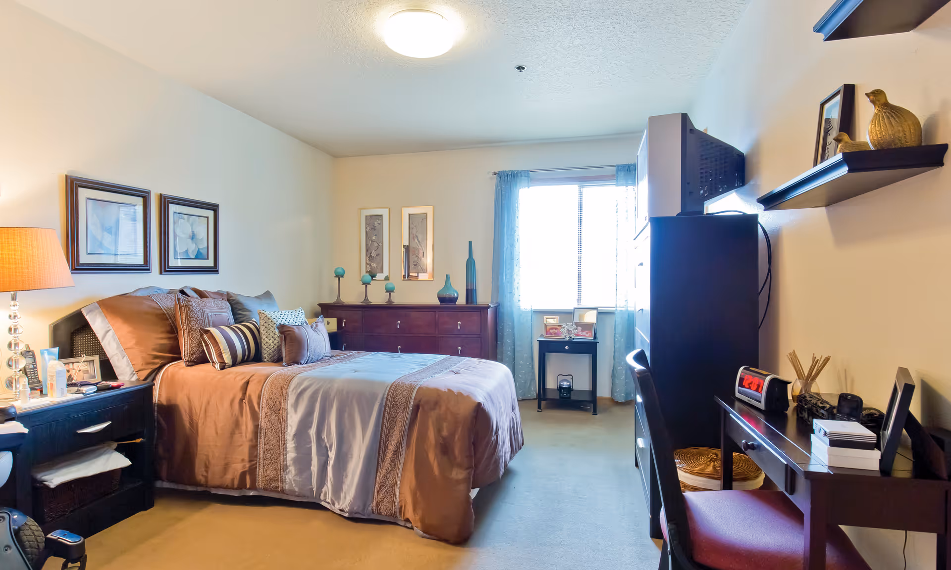 A well-furnished Brookdale Forest Grove bedroom with bed, dresser, desk, and wall decor.